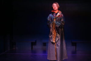 Cedric mit silbernem Mantel gekleidet stehend auf der Bühne.